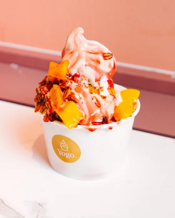 Vaso de helado de yogurt con mango, granola y jarabe de fresa