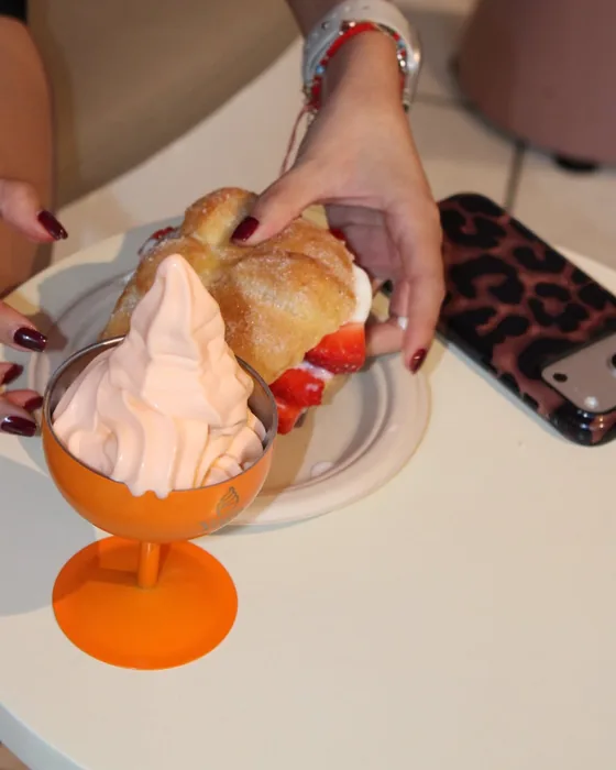 Pan de muerto relleno de helado de yogurt y fresas junto a una copa naranja